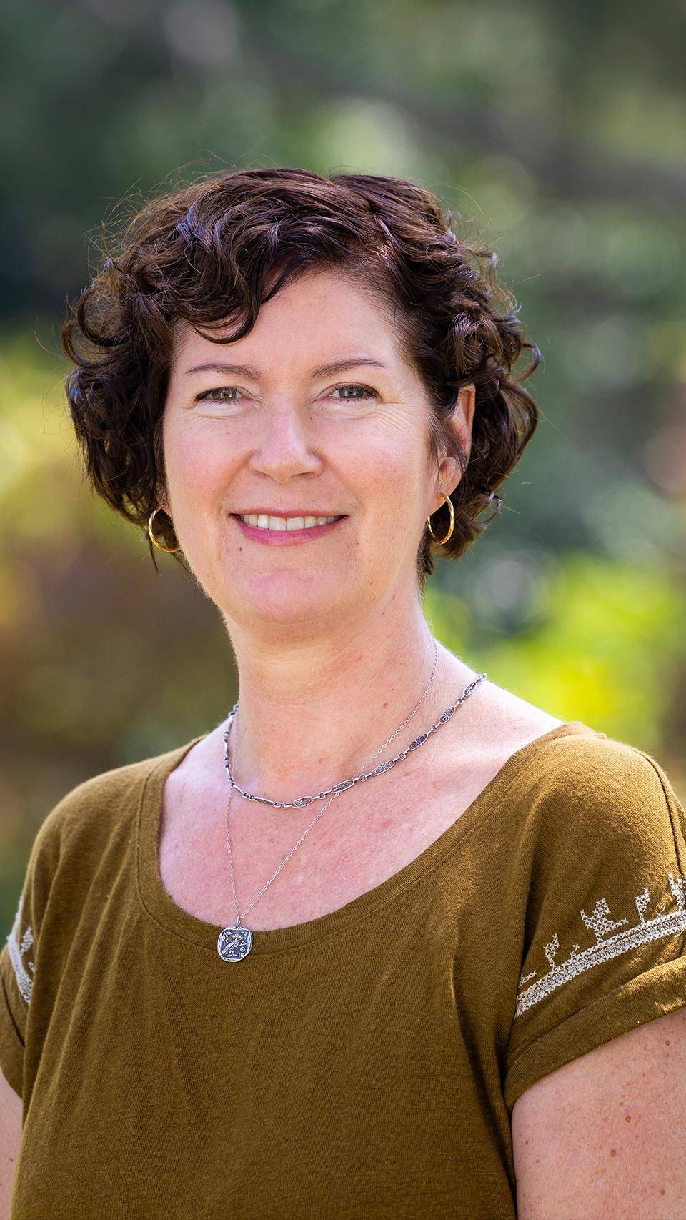 a person with short curly hair wearing a green shirt and gold earrings