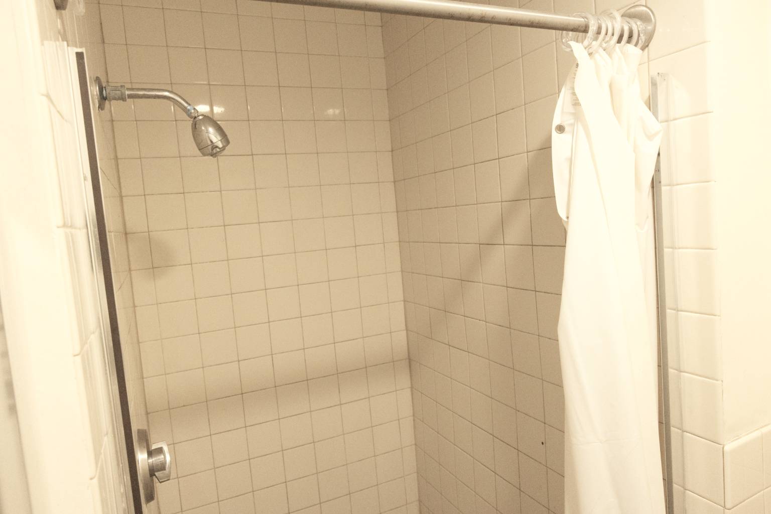a shower with a shower head and a white shower curtain