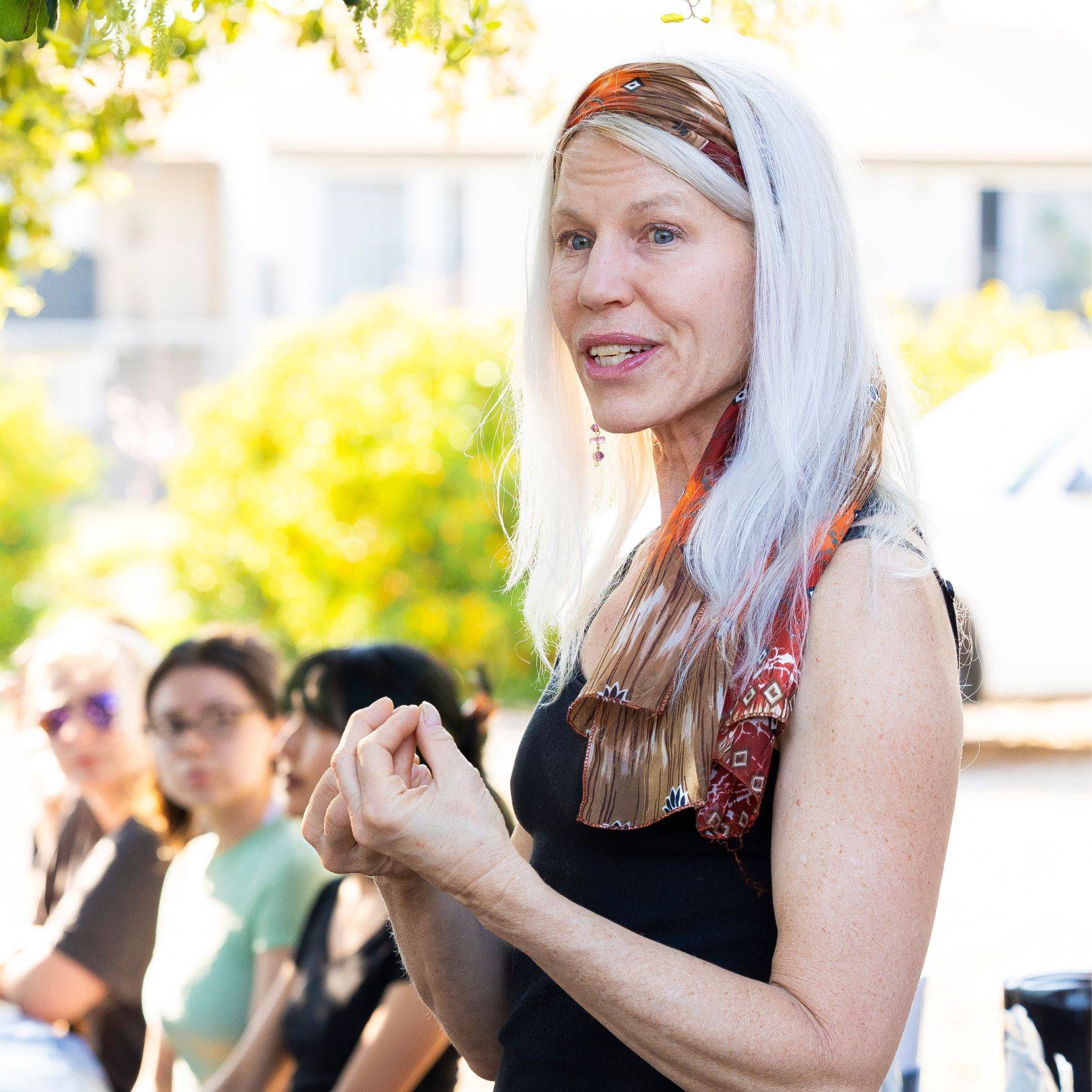 a person with white hair and a scarf standing in front of a group of people