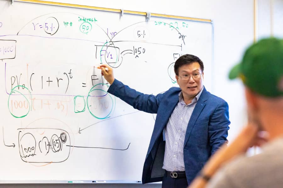 a person in a suit pointing at a whiteboard