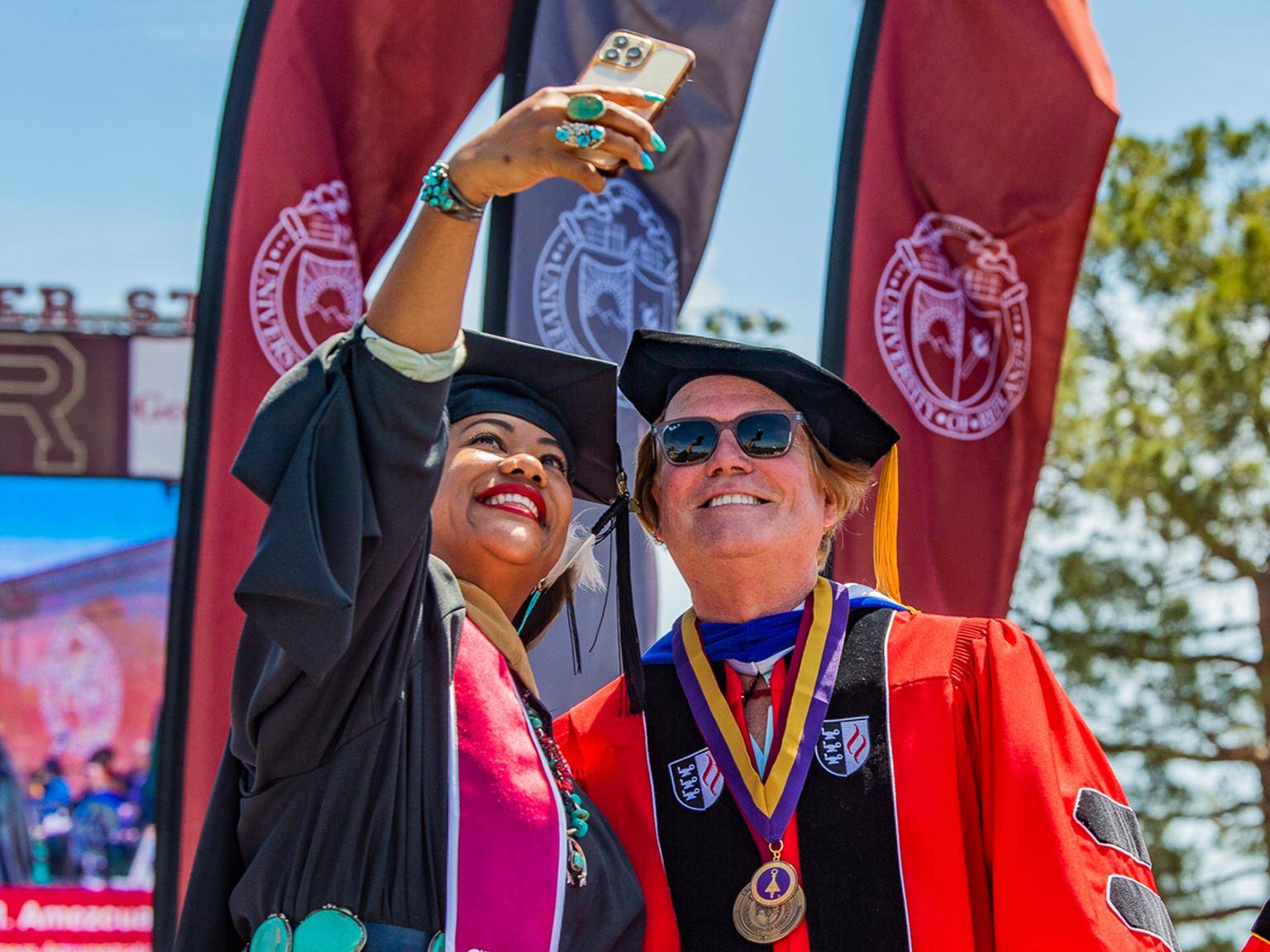 a person taking a selfie with a person in graduation gown