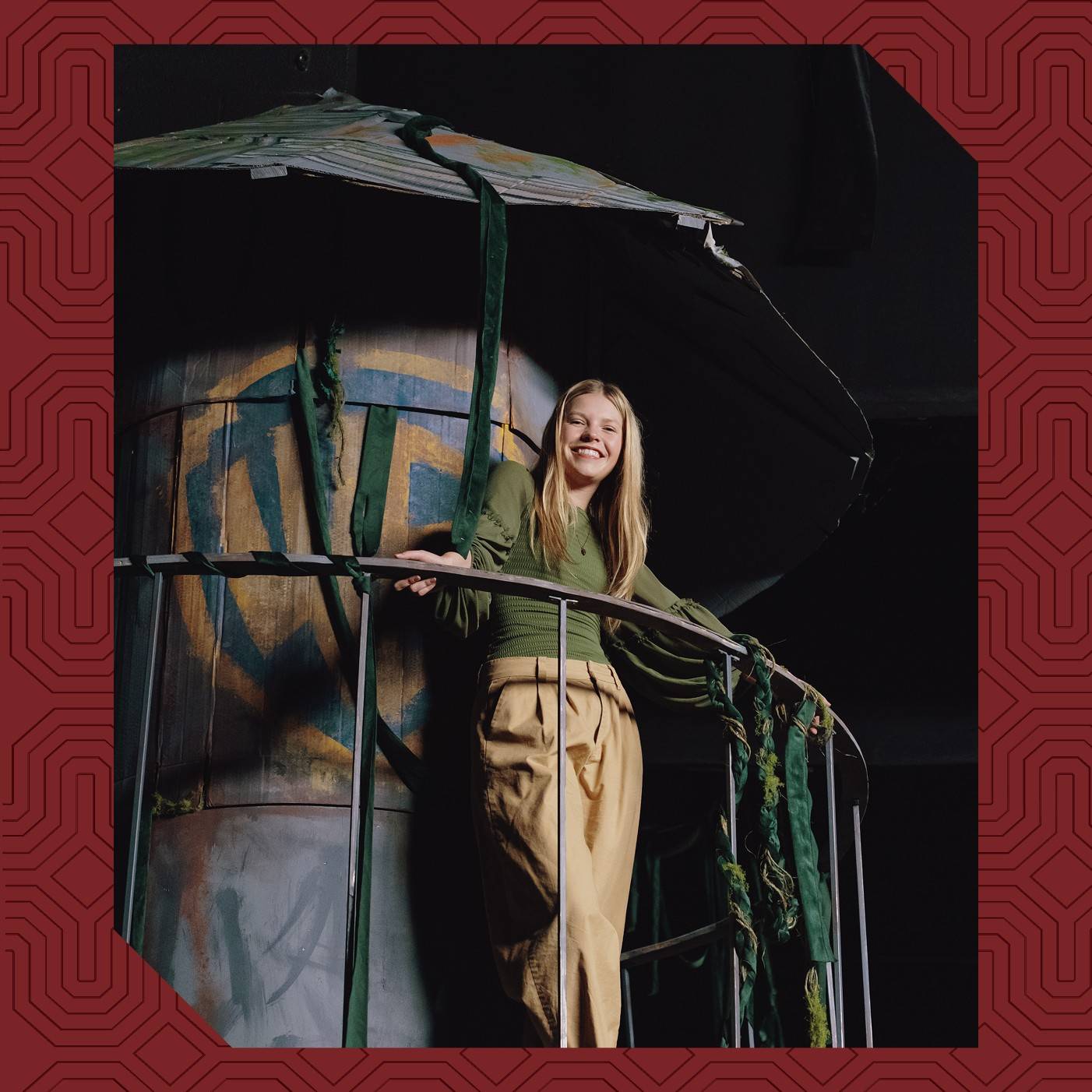 Studio art major Avery Heidebrecht ’26 standing on the metal railing of the Warner Brothers Water Tower set piece she designed.