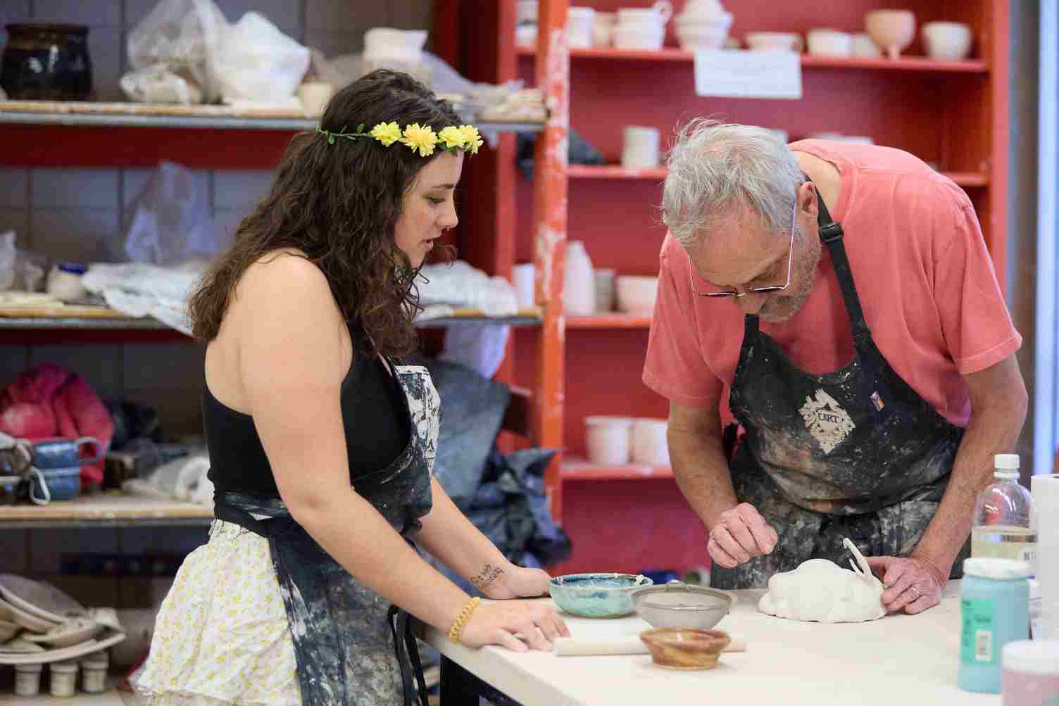 Student and teacher in aprons working on a pottery project