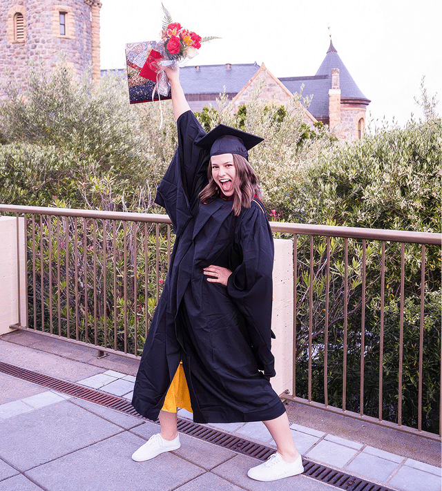 a person in a graduation gown and cap holding a bouquet of flowers