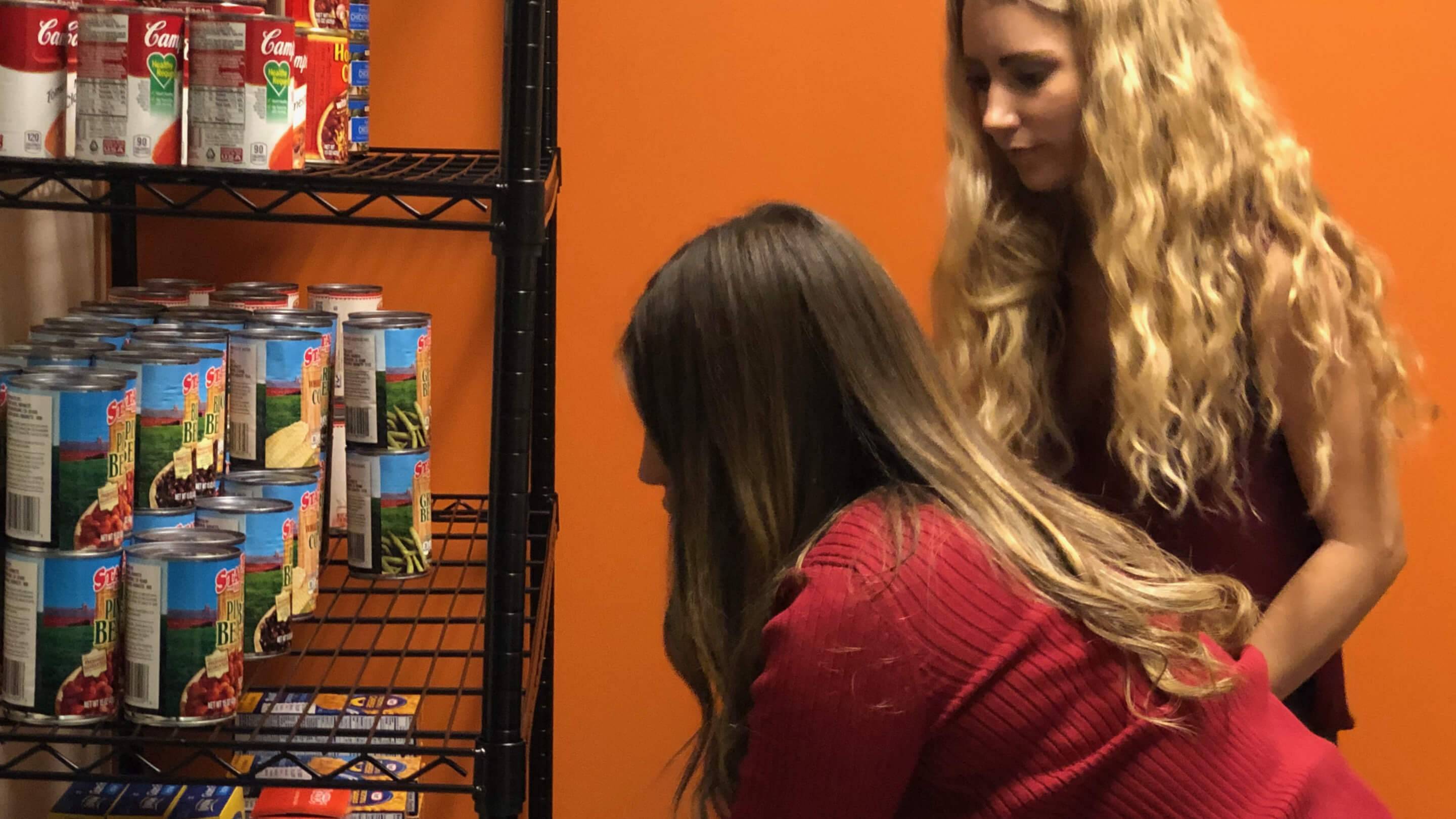 a person with long hair sitting next to a shelf with cans of food