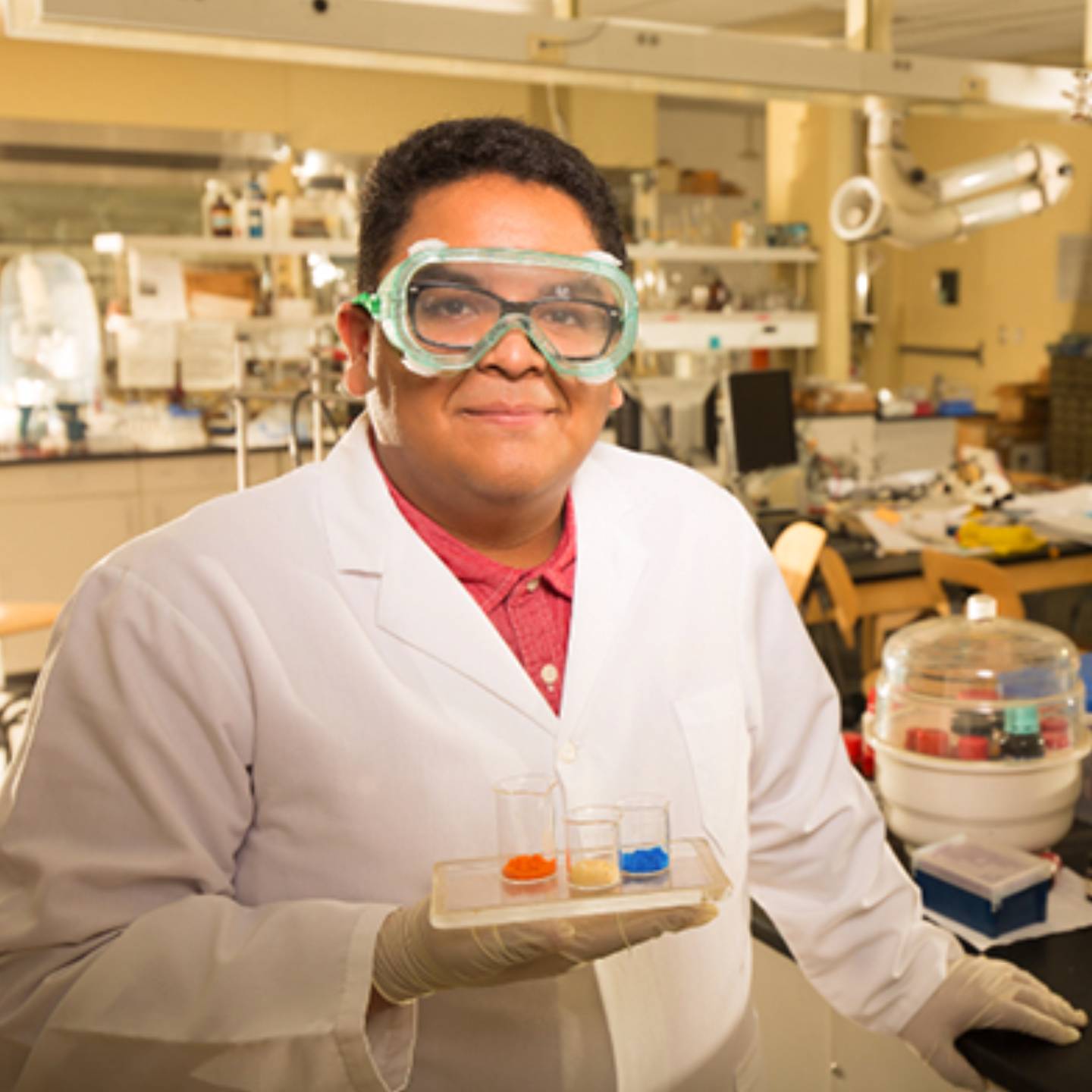 a person wearing a white coat and goggles holding a tray of test tubes