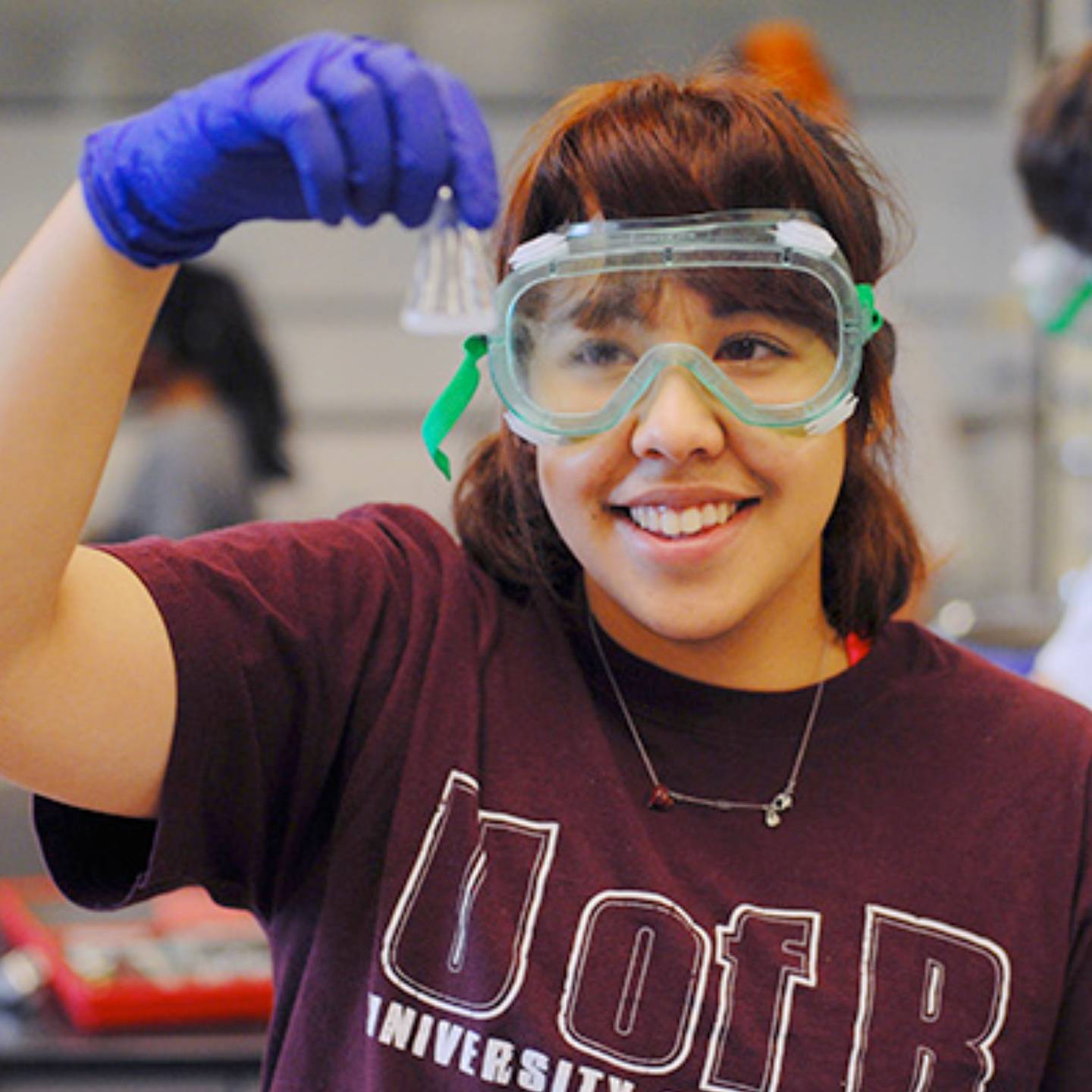 a person wearing safety goggles and gloves holding a beaker