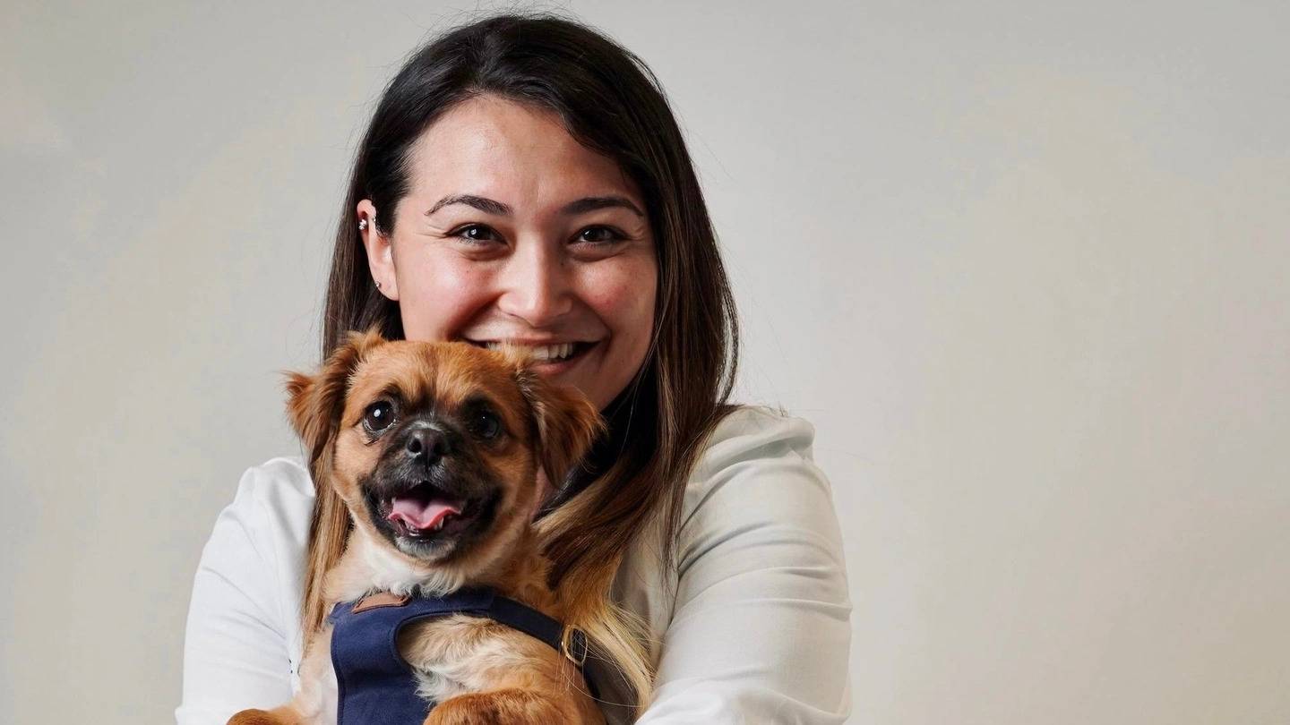 A University of Redlands alumna holding a brown dog in front of her.