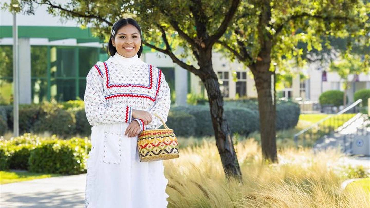 A student in a white dress holding a woven basket