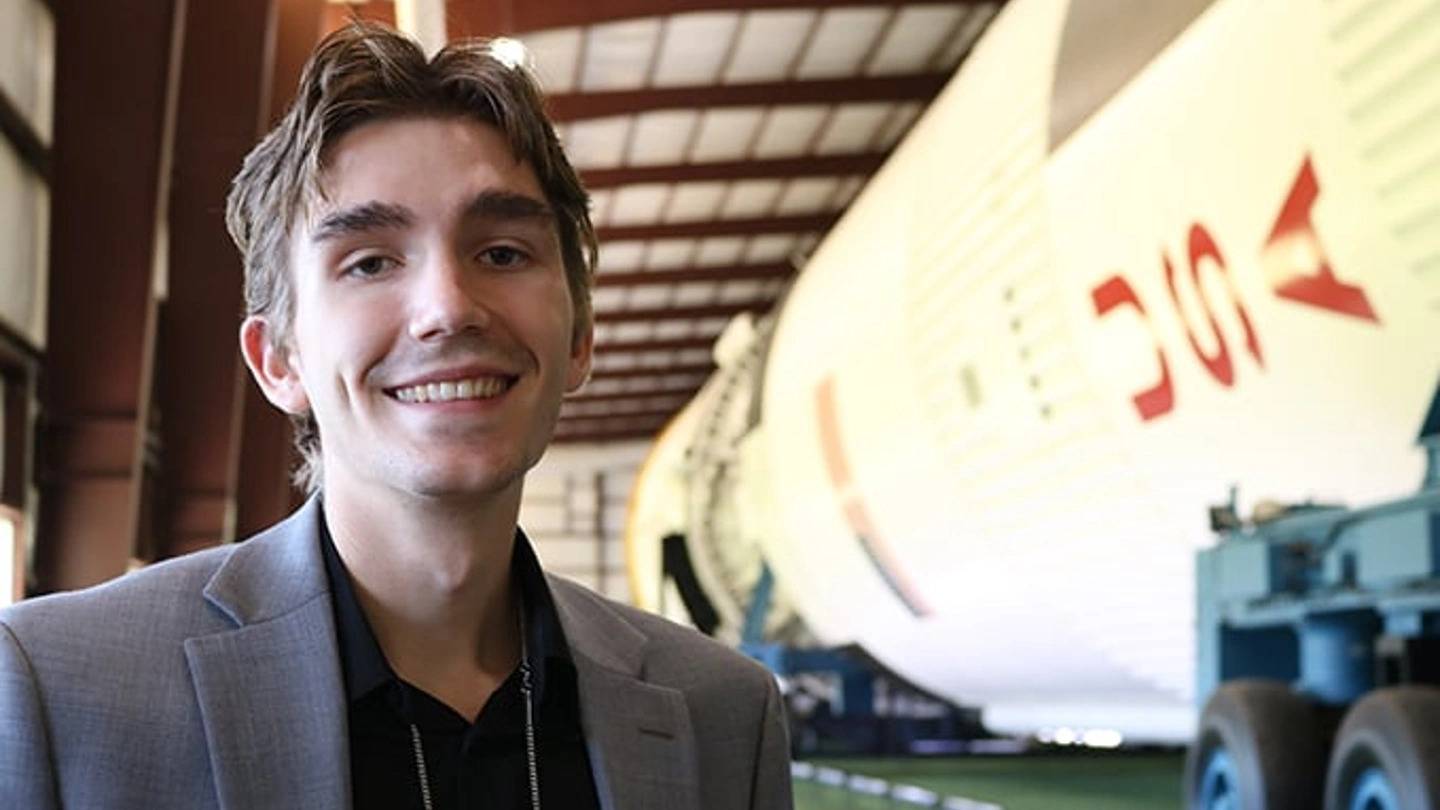A student smiling in front of a white rocket
