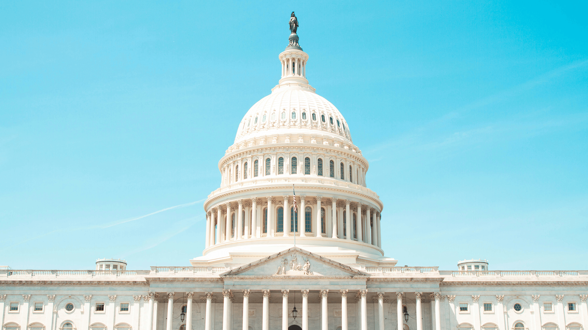 a white building with columns and a statue on top with United States Capitol in the background