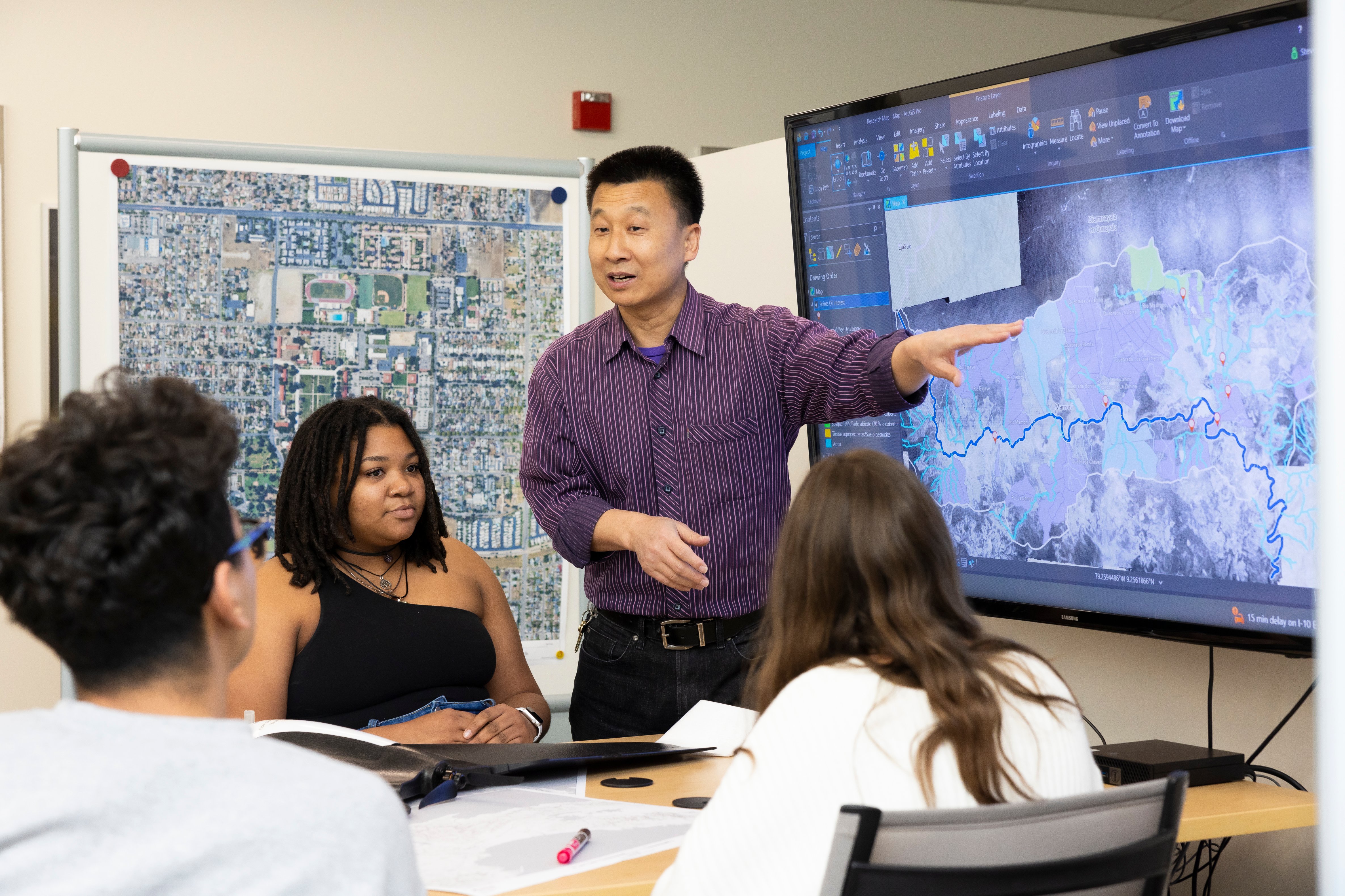 a man pointing at a screen with people sitting around it