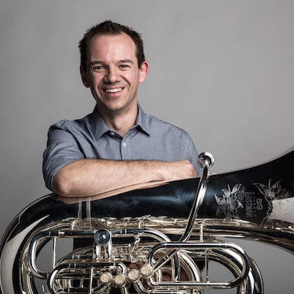 a person smiling with his arms crossed and a tuba