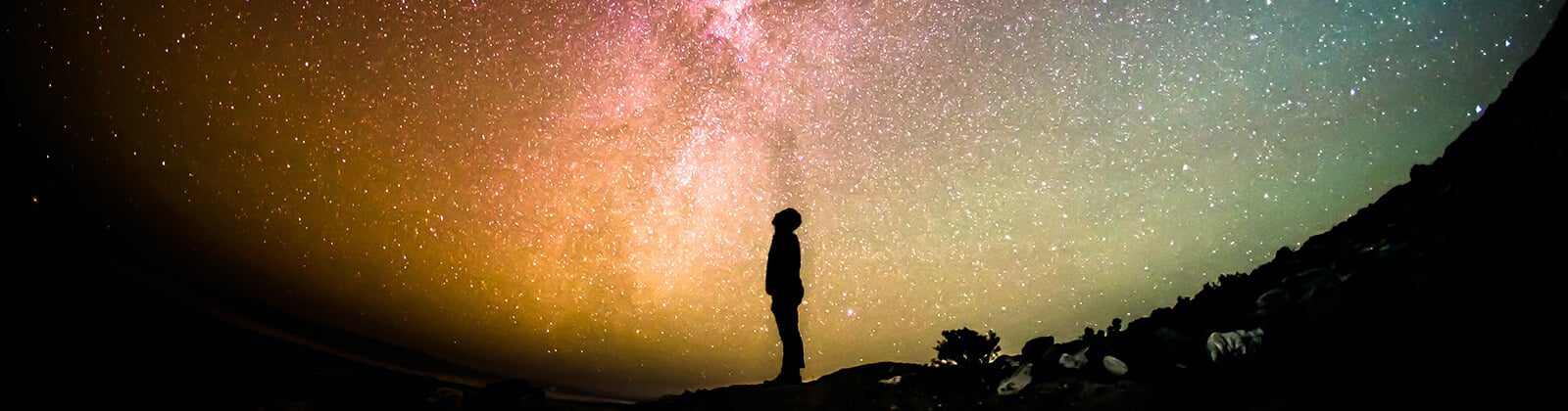 a silhouette of a person standing on a hill with stars in the sky