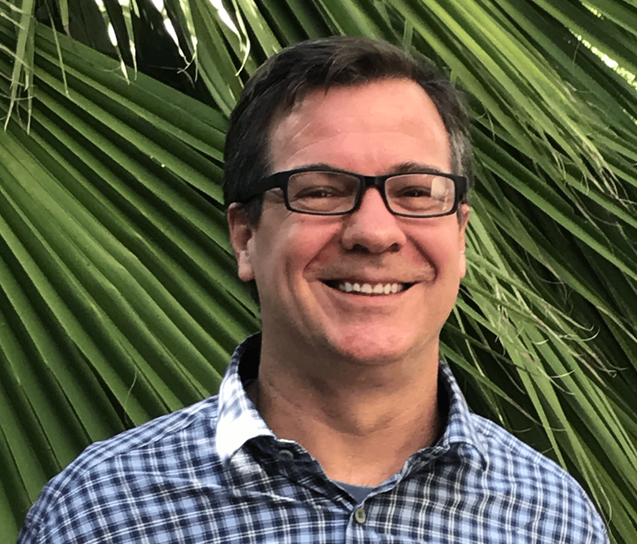 a man smiling in front of a palm tree