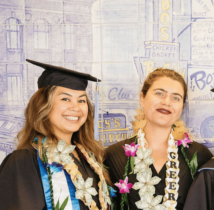 two women wearing graduation gowns and leis