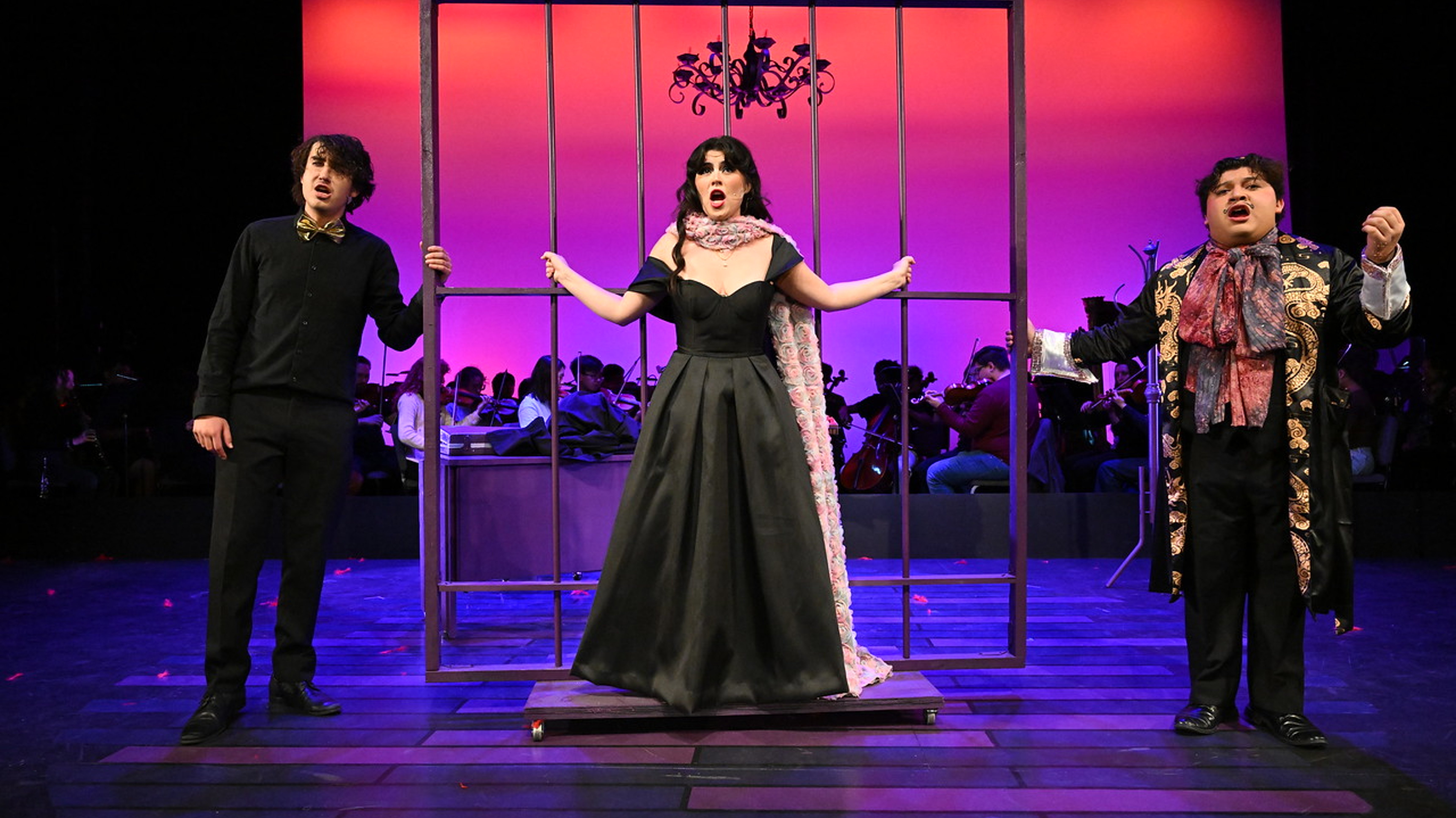 a person in a black dress standing in front of a cage with a group of people behind her