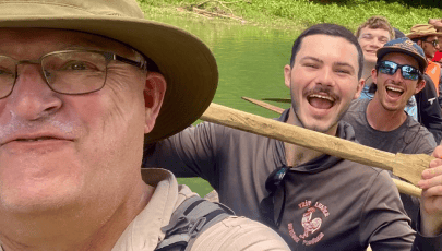 a person in a hat and glasses with a stick in front of a person in a boat