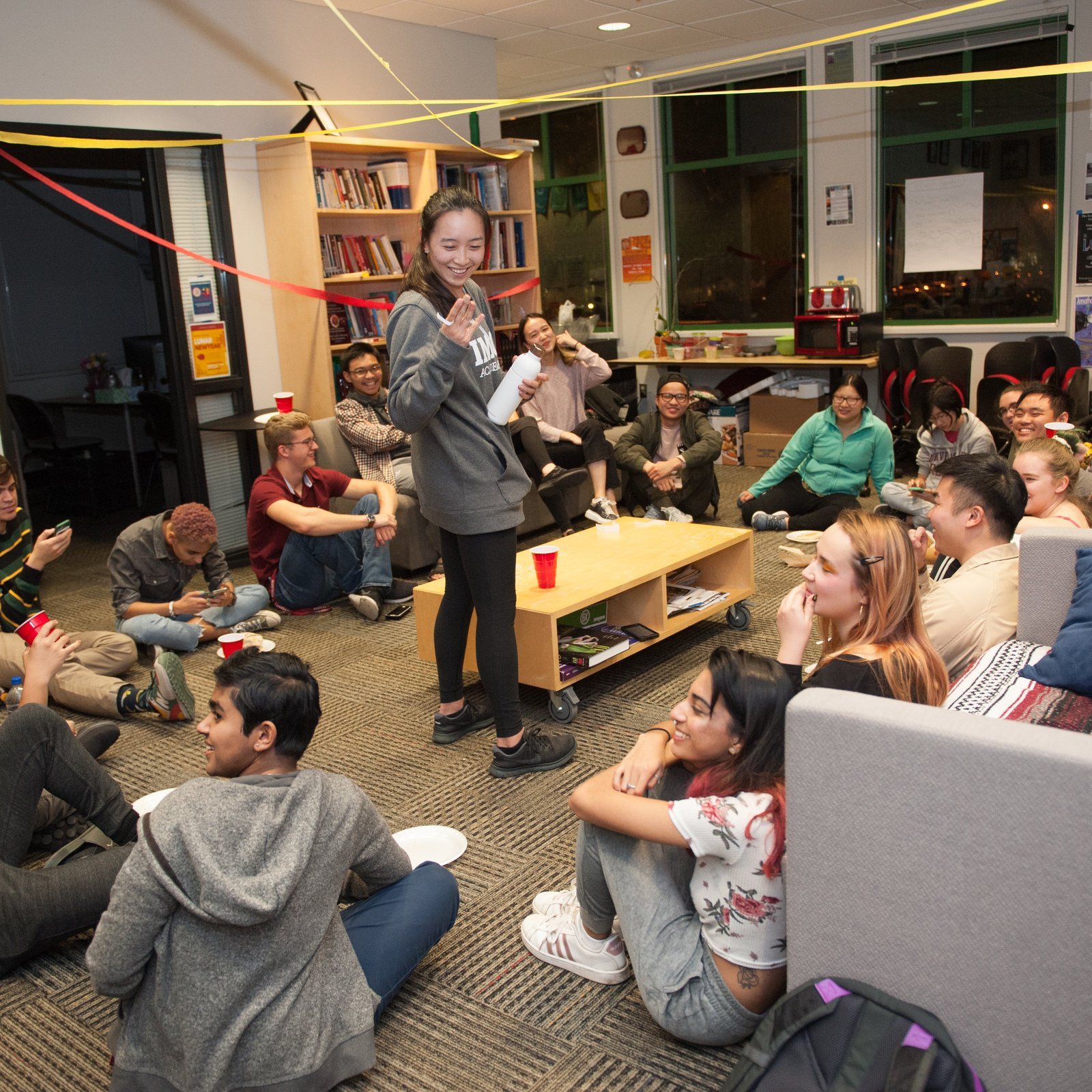 a person standing in a room with a group of people sitting on the floor