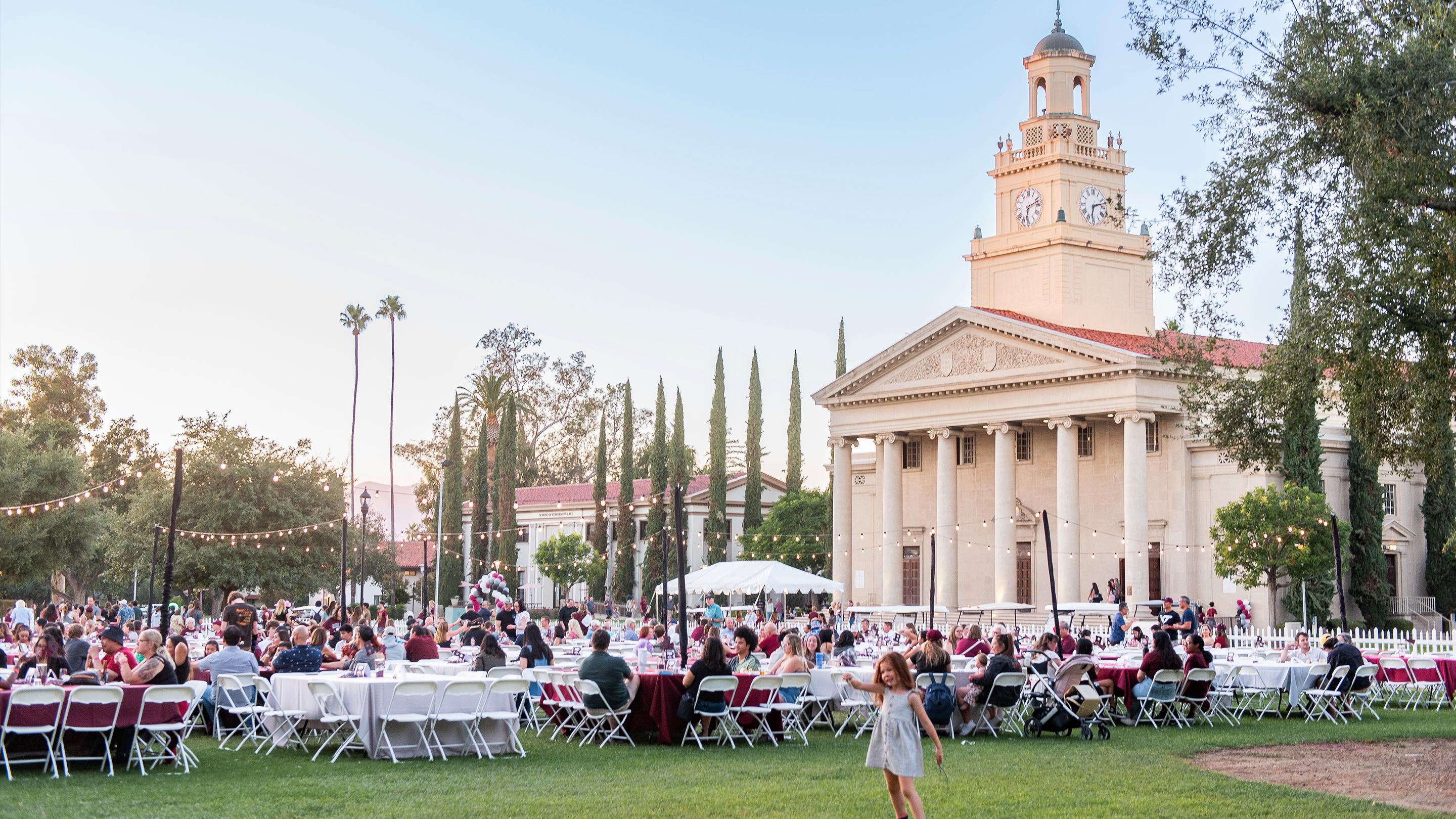 a large group of people sitting in a lawn outside a building
