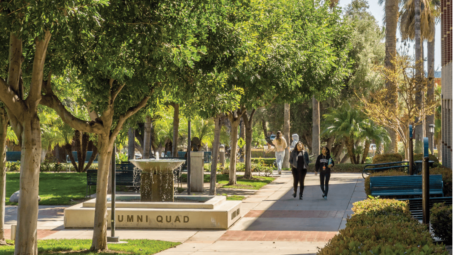 people walking on a sidewalk with a fountain and trees