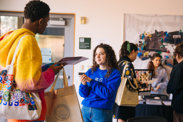 Two students speaking to each other, with more students grouped behind them interacting.