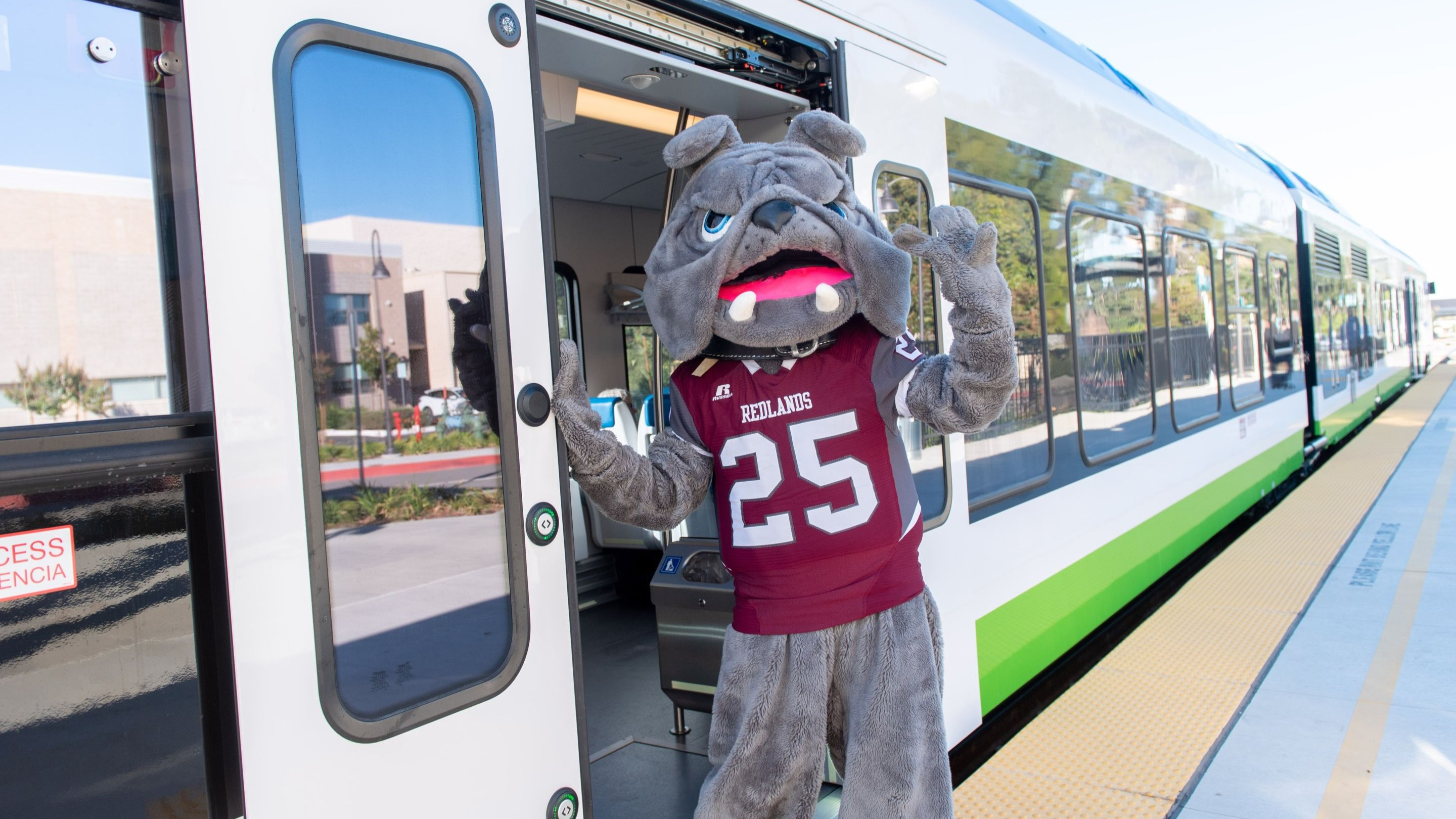 University of Redlands Bulldog mascot standing in the doorway of a Metrolink Arrow train at a station platform.