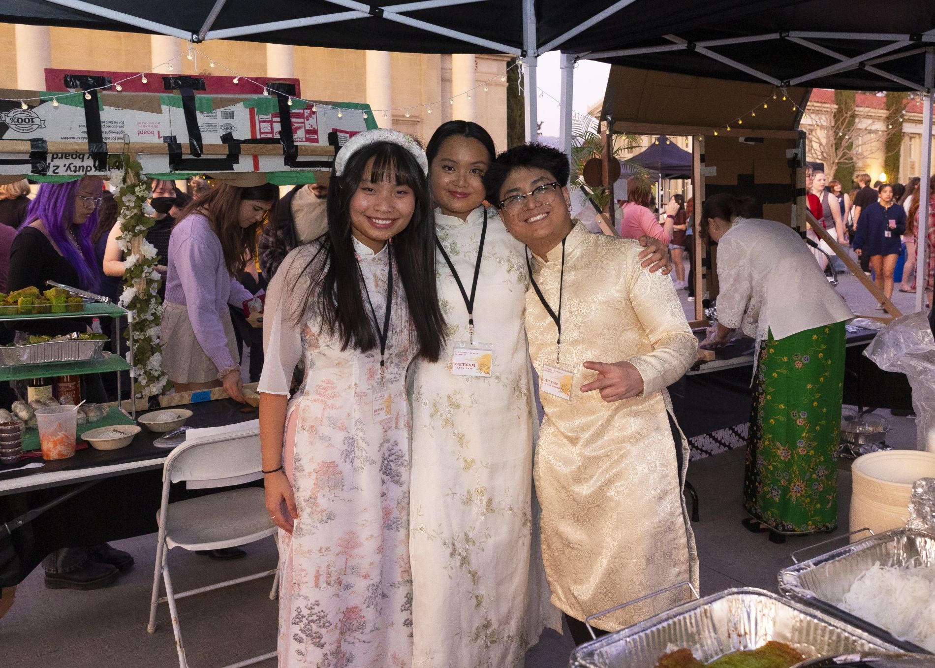 Three students stand together in traditional attire at a booth during the Asian Student Association Night Market.