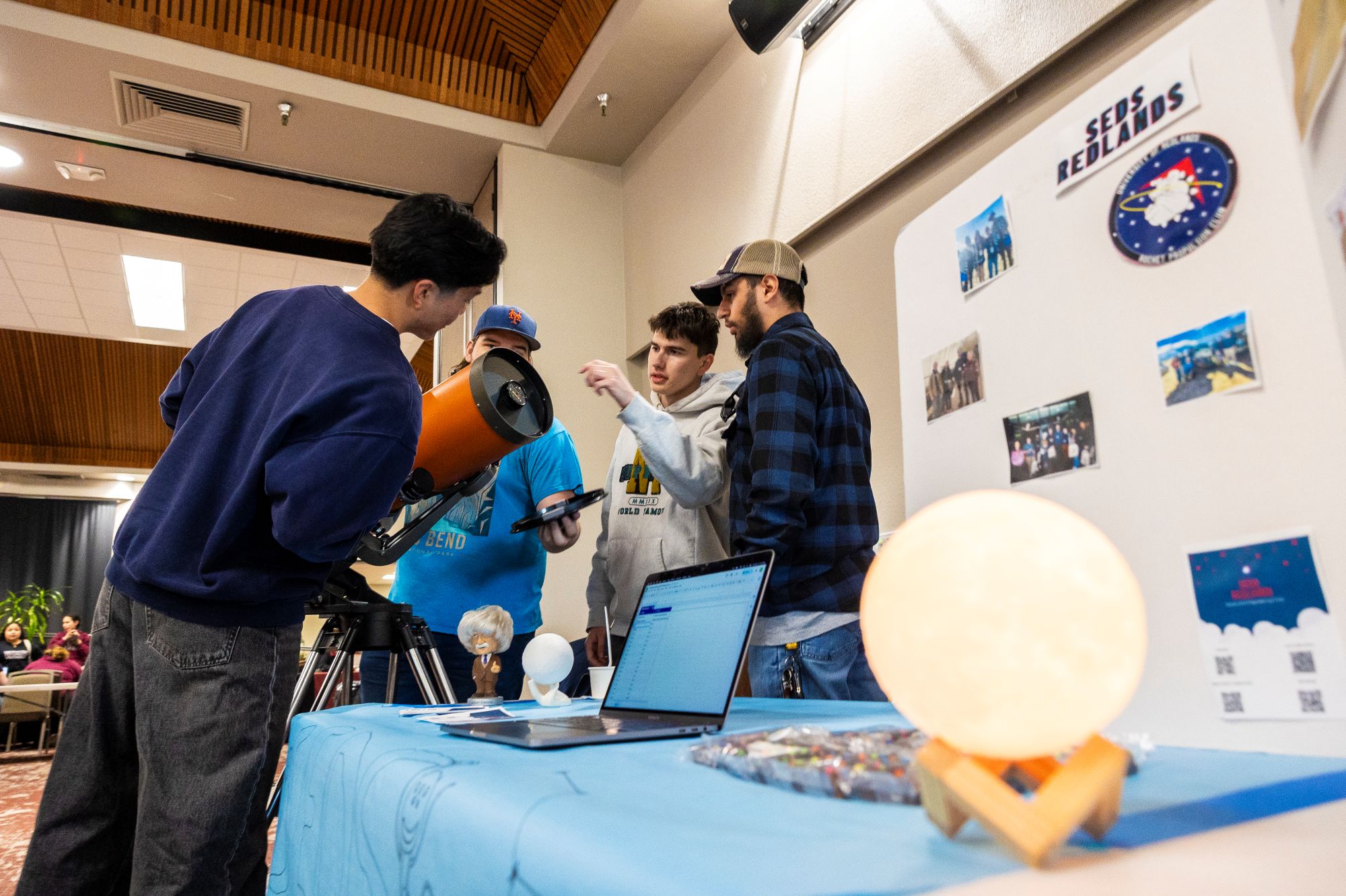 A group of students examine an orange telescope at an Involvement Fair club booth.